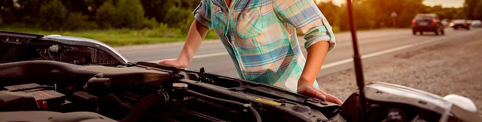 Driver leaning over the open hood of a broken-down car on the side of the road