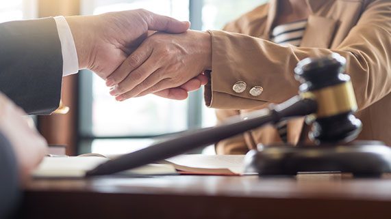 Client and attorney shake hands over a gavel and case file